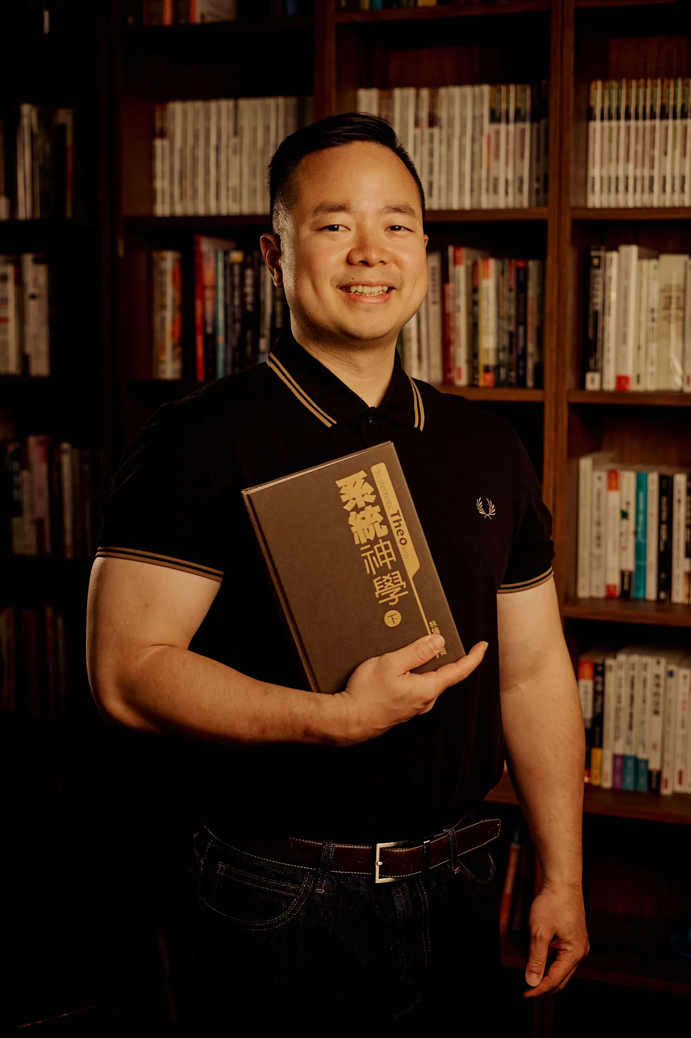 Andrew Yang holding a systematic theology volume in front of his book wall